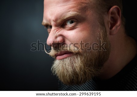Profile of frightening bearded man on black. Man with serious glance looking with wickedness and narrowing his eyes.