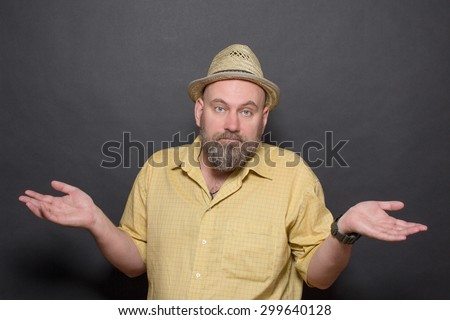 Portrait of being surprised bearded man on dark grey background. Bold man in yellow shirt shrugging his shoulders.