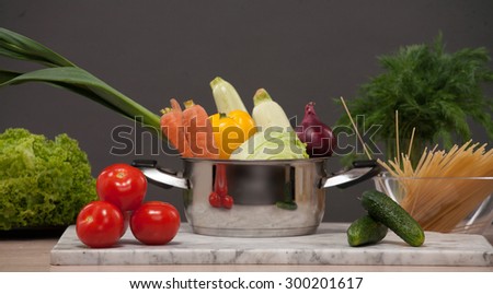 Close-up picture of still-life with fresh vegetables on the counter. Pan full of carrot, red onion, cabbage, leek represented in the centre.