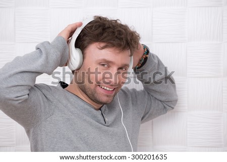 Handsome man wearing white earphones isolated on white. Short-haired man in grey sweater smiling for the camera.