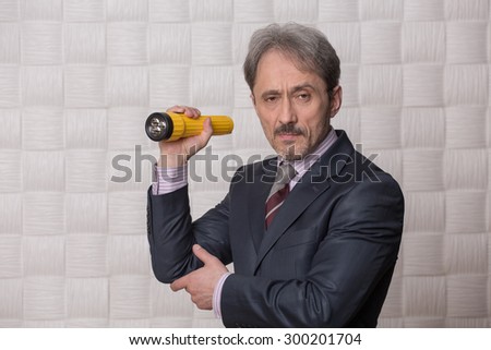 Mature businessman posing with yellow-coloured flashlight in his hand. Serious man is going to clear up the situation connected with low profit.