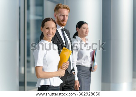 Three businesspeople welcoming you. Woman in white shirt with yellow folder smiling isolated on her collegues.