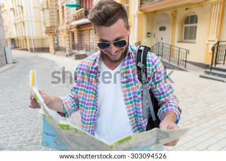 Attractive hipster man in sunglasses looking at city map. Man in plaid shirt with backpack looking for directions.