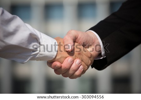 Business handshake, the deal is finalized between two enterprises. Man in black suit and woman in white one have signed the agreement.