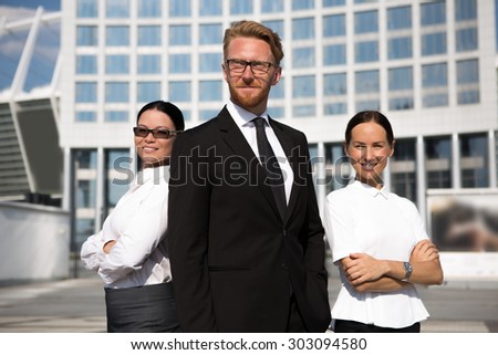 Successful smiling businessman in suit standing in front of his colleagues. Smiling businesswomen in white shirts posing with arms crossed.