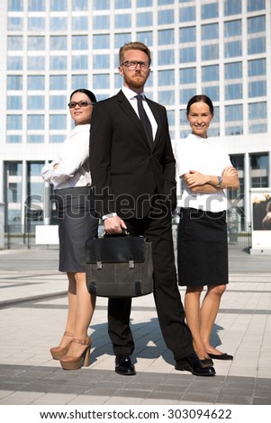 Photo of businesspeople in full length isolated on office building. Man in glasses posing with brief case, businesswomen with arms crossed.