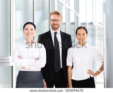 Group of businesspeople standing together. Man in business suit with his collegues women in white shirt smiling.