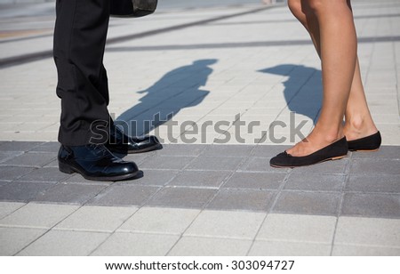Two business partners standing face to face. Businessman in black suit telling smth to his business partner woman.