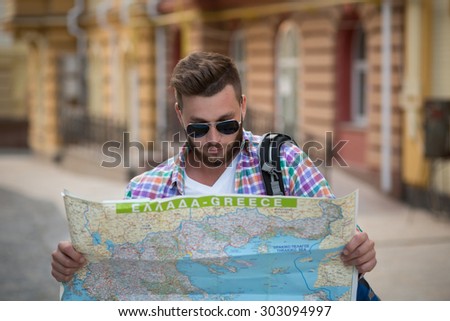 Young hipster man with map outdoors. Serious man with backpack going to find interesting sightseeings in the city.