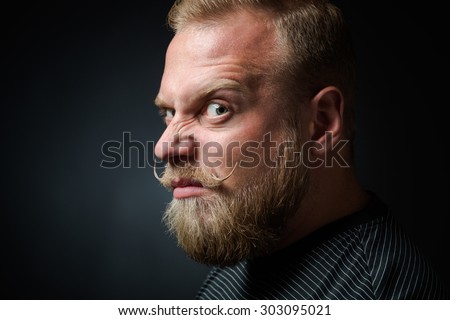 Profile of demanding blond bearded man on black background. Serious man looking so strange and narrowing his eyes because of annoyance.