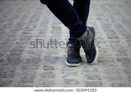 Man standing with his legs crossed. Close-up of model\'s legs in casual black jeans and feet in black sneakers.