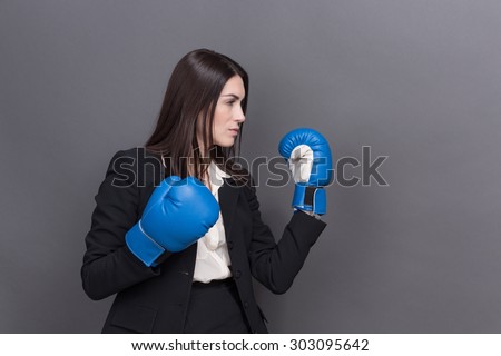Business lady in blue with white boxing gloves isolated on grey. Long-haired woman in black business suit ready for fight.