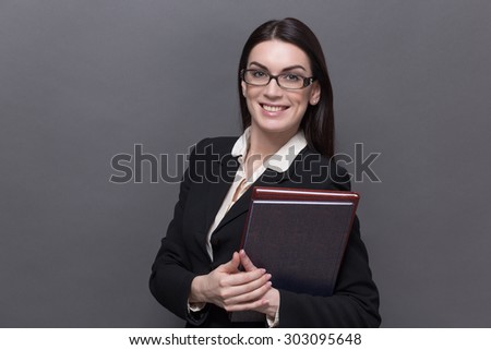 Business lady smiling in glasses. Pretty model in black business suit carrying documents and files in her hand.