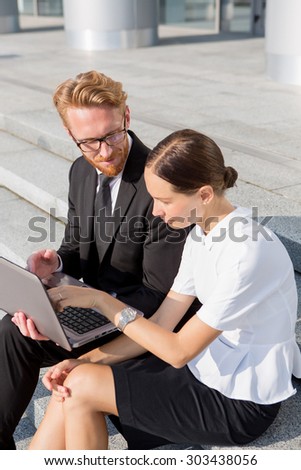 Business people sitting near office building with laptop. Smart businesswoman asking questions in his colleague near by.