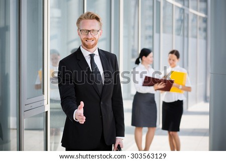 Portrait of successful handsome businessman giving a hand. Smiling man in glasses and black suit ready to have a deal with you.