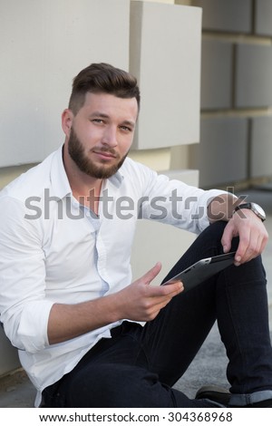 Profile of bearded handsome man freelancer working on tablet PC. Serious man sitting near building with tablet pc.