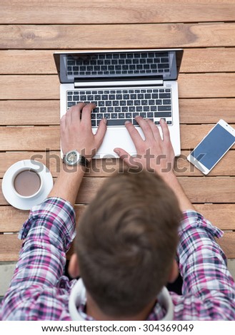 Close-up portrait of man\'s hands typing on laptop. A cup of coffee with milk on the left and smart phone is on the right isolated on wooden table.