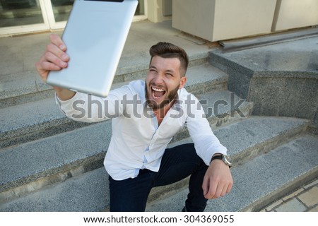 Man freelancer communicating with his foreign friends outdoors using tablet PC. Handsome man in white shirt posing for the camera.