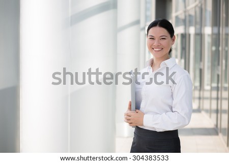 Asian businesswoman isolated on the territory of enterprise. Beautiful lady in white shirt smiling with file in her hands.