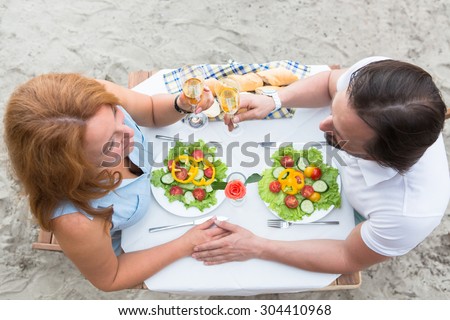 Dating concept of mature couple in the restaurant by the sea or river. Man and woman holding hands and sitting face to face.