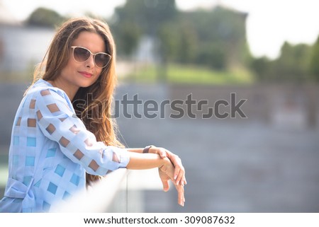 Attractive lady in sunglasses standing on the bridge and looking at the camera. Pretty lady spending her weekends outside.