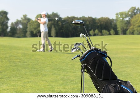 Golf equipment. Golf clubs in golf bag on the foreground, man playing golf on the background during summer vacation.