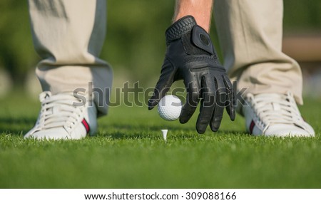 Close-up picture of man's hand holding golf ball with tee on course. Professional golfer playing golf over green field course.