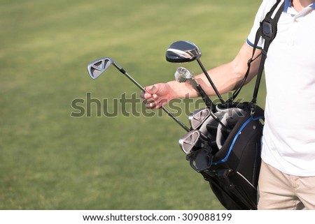Golf and golfer concepts. Man in white T-shirt removing a driver from golf bag. He is going to spend his time on golf green course.