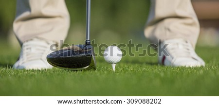 Golfer getting ready to hit the ball. Professional male golf player going to hit a ball by a driver from tee on green course.