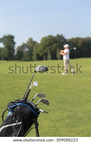 Close-up picture of golf clubs in golf bag isolated on green field background. Man playing professional golf on the background.