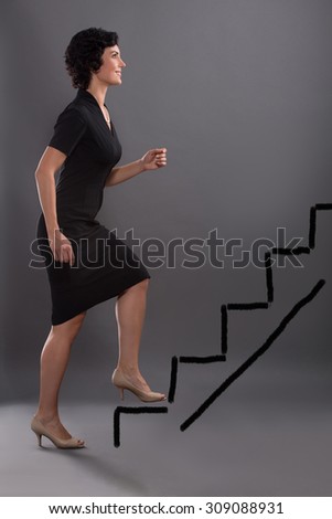 Career advancement concept. Business woman stepping up on stairs to gain her success with grey wall background.