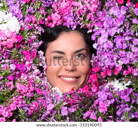 Beautiful woman winking among lilac flowers. Black-haired woman smiling, laughing and showing her teeth.