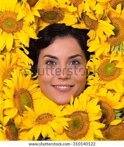 Beautiful smiling woman\'s face represented in the frame from sunflowers. Black-haired woman demonstarting her perfect skin.
