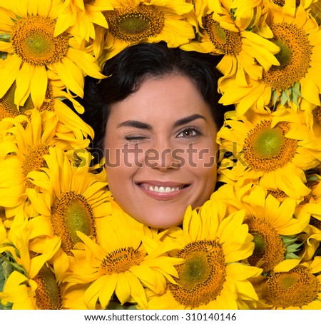 Beautiful woman winking. Lady\'s face represented in the frame of sunflowers. Woman is smilimg, laughing and showing her teeth.