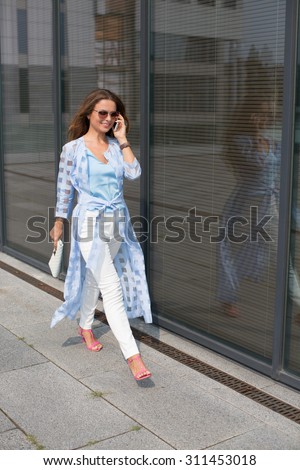 Happy businesswoman walking to her job and talking over mobile phone with partners. Smiling lady with red lips discussing business moments.