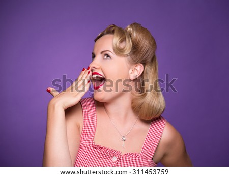Happy surprising pin-up girl looking away and closing her mouth. Blond lady with red lips posing for photographer isolated on violet background.