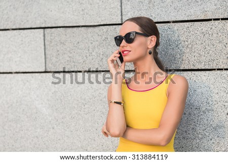 Happy fashion girl speaking over mobile phone near brick wall of building. Lady with red lips discussing burning issues with her friends.