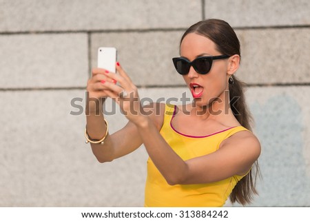 Fashion girl making selfies vogue photos. Pretty girl with long brown hair looking at the camera. Woman with red lips holding mobile phone in front of her.
