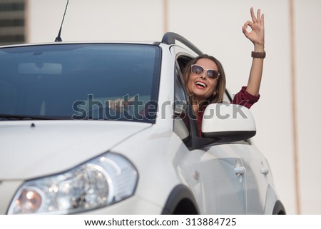 Gorgeous businesswoman showing her satisfaction by new car she bought. Lady in sunglasses with okay sign up smiling from the window of her car.