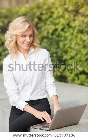 Freelance lady working in the park with her laptop computer. Smiling lady typing the document and enjoying her working time outdoors.