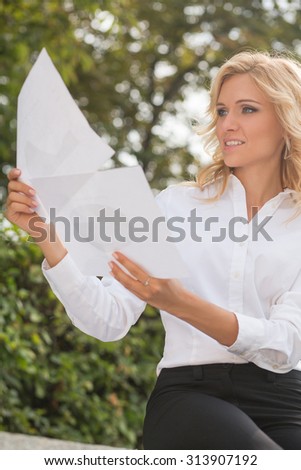 Portrait freelance lady comparing the documents. Beautiful woman working oudoors. She is holding papers in front of her.
