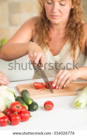 Close-up picture of red-haired woman cutting tomatoes for vegetables salad. Pretty lady working in the kitchen.