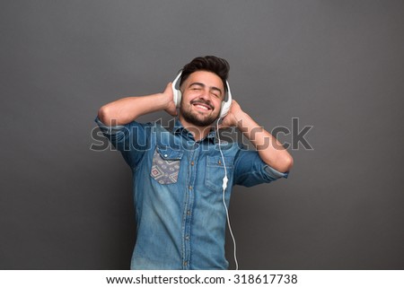 Handsome hipster man listening to the music in his white earphones. Man in jeans shirt enjoying different modern tracks.