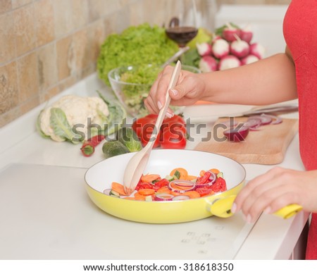 Fresh vegetables on the pan are being mixed by housewife on electric cooker. Woman stirring them with the help of big spoon in the kitchen.