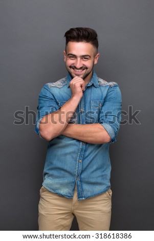 Thoughtful handsome hipster man touching his chin. Bearded man in jeans shirt and cream trousers smiling for the camera and looking straight.