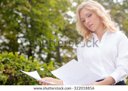 Serious freelance lady reading the documents. Blonde likes working oudoors in the park. It is nice time to concentrate.