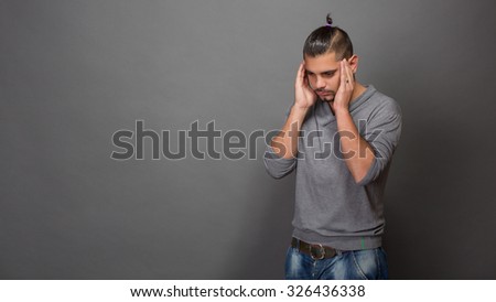 Fashionable hipster man touching his head with both hands. Young man with modern hairstyle looking down and thinking about something in studio.