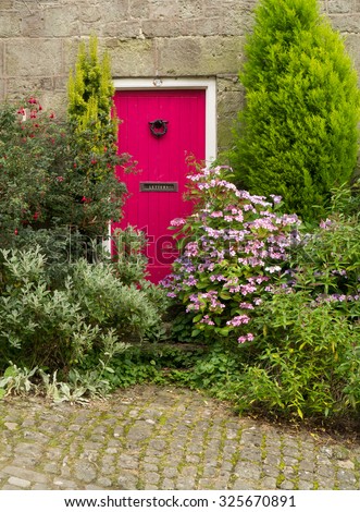 a vivid pink door on a stone cottage, surrounded by shrubbery