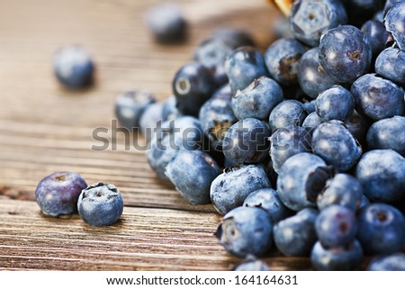 Fresh blueberries scattered on the wooden table. Shallow depth of field, focus on left berry.