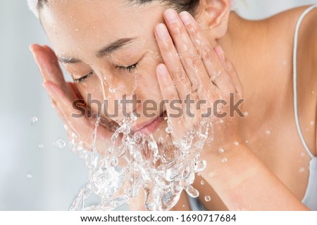 Young woman washing face in room.